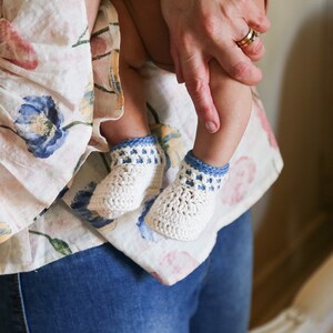 May include: A person holding a baby wearing white crocheted booties with blue trim.