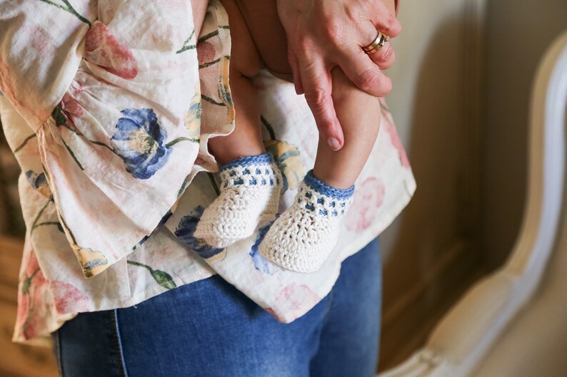 May include: A person holding a baby wearing white crocheted booties with blue trim.
