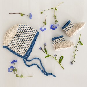 May include: A crocheted baby bonnet and booties set in white and blue. The bonnet has a scalloped edge and ties under the chin. The booties have a blue and white striped pattern.