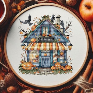 Puede incluir: Un bastidor de bordado de punto de cruz con un diseño de casa de Halloween, calabazas, cuervos y la palabra "Halloween". La imagen está rodeada de hojas de otoño, manzanas, palitos de canela y una taza de té.