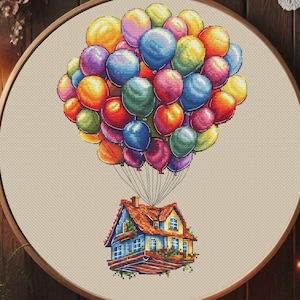 Puede incluir: Un bordado de punto de cruz de una casa elevada por globos de colores. La casa tiene una fachada azul y amarilla con un tejado rojo. Los globos son de color rojo, naranja, amarillo, verde, azul y morado. Enmarcado en un marco de madera redondo.