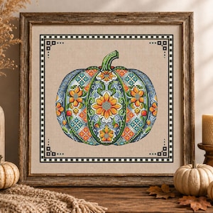 May include: A framed cross-stitch embroidery featuring a central pumpkin design with intricate patchwork-style floral patterns in orange, blue, and green. The artwork is enclosed in a wooden frame with a black and white checkered border.