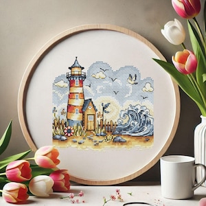 May include: A framed cross-stitch depicting a coastal scene. The artwork features a lighthouse with red and yellow stripes, a small building, and a crashing wave. The sky is blue with fluffy clouds and flying birds. The frame is round and made of light-colored wood.