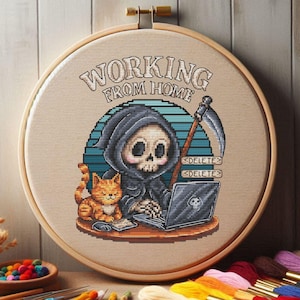 Puede incluir: Un bastidor de bordado de punto de cruz con un dibujo de la Muerte trabajando en un portátil con un gato. El texto "WORKING FROM HOME" está arqueado encima de la escena. La Muerte sostiene una guadaña y el portátil tiene un logotipo de calavera.