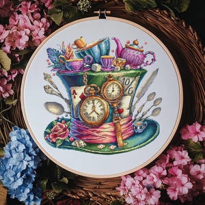 Könnte beinhalten: Kreuzstich-Stickrahmen mit einem verspielten Design, inspiriert von Alice im Wunderland. Das Design umfasst einen grünen Zylinder, Taschenuhren, Teetassen, Spielkarten und eine rosa Rose, alles vor einem floralen Hintergrund.