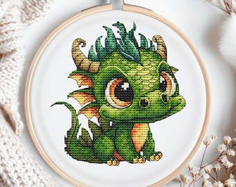 Può includere: Ricamo a punto croce di un drago verde con occhi grandi e un corno giallo. Il drago è seduto su uno sfondo bianco.