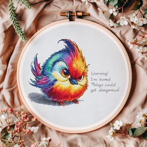 May include: A colorful cross-stitch embroidery of a cartoon bird with the text "Warning! I'm bored. Things could get dangerous!"