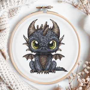 May include: A cross-stitch embroidery of a cute, cartoon dragon with large, green eyes. The dragon is sitting on its hind legs with its wings spread out. The dragon is black with brown accents.