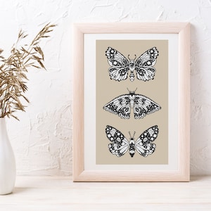May include: A framed print with three black and white butterfly illustrations on a beige background. The butterflies are arranged vertically, with the largest butterfly at the bottom.