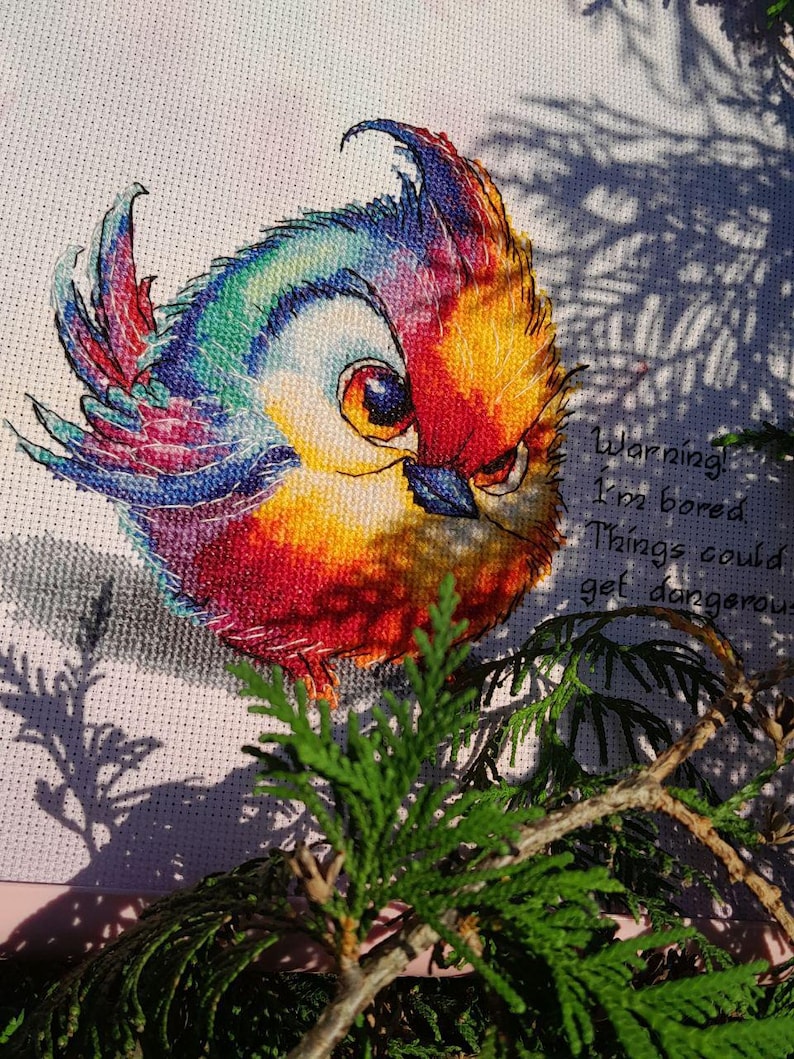 May include: A colorful cross-stitch embroidery of a bird with the text "Warning! I'm bored. Things could get dangerous."
