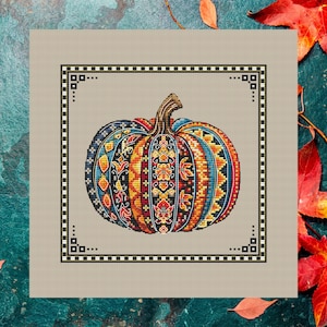 May include: A cross-stitch design of a pumpkin with a detailed pattern in shades of blue, orange, red, and yellow. The pumpkin is centered within a square frame with a black and white geometric border, set against a neutral background.