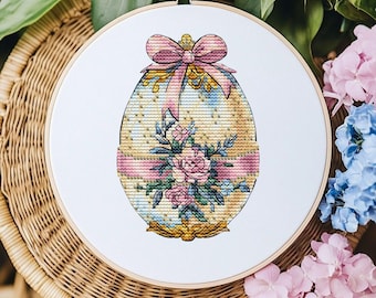 May include: A white embroidery hoop with a cross-stitch design of a pastel yellow Easter egg decorated with pink and blue flowers and a pink bow.