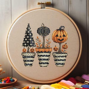 May include: A cross-stitch embroidery featuring three Halloween-themed potted plants. The plants include a black and white tree, a black pumpkin, and an orange jack-o'-lantern. The embroidery is set in a wooden hoop, perfect for seasonal decor.