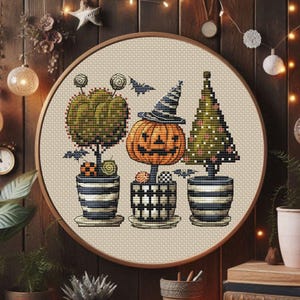 Può includere: Un disegno a punto croce in una cornice rotonda di legno presenta tre piante in vaso a tema Halloween. La pianta centrale è una zucca arancione con un cappello da strega. Le altre piante sono un'arte topiaria e un albero di Natale.