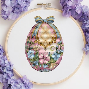 Könnte beinhalten: Ein rosa Osterei mit goldener Verzierung und einer blauen Schleife. Das Ei ist mit blauen und rosa Blumen und grünen Blättern verziert.