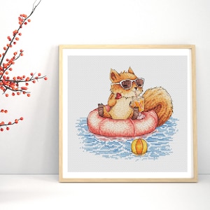 May include: A cross-stitch pattern in a light wooden frame featuring a brown squirrel wearing black sunglasses, floating on a pink inflatable ring in blue water, holding a drink with a straw and a small red fruit, with a yellow beach ball nearby.