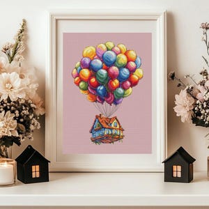 Peut inclure: Une œuvre d'art au point de croix encadrée représente une maison suspendue par un groupe de ballons colorés. Les ballons sont dans les tons de rouge, orange, jaune, vert, bleu et violet. La maison a un toit et des murs bleus, avec un toit marron.