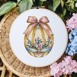 Op de afbeelding: Een borduurring met een kleurrijk paasei-ontwerp. Het ei is versierd met een roze strik, gouden accenten en bloemmotieven.