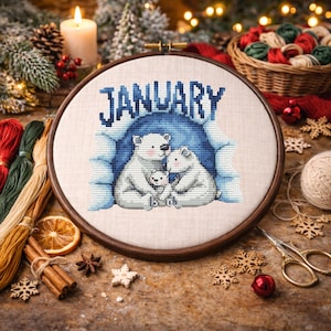 May include: A cross-stitch embroidery hoop featuring a polar bear family inside a blue cave, with the word "JANUARY" above. The hoop is set against a festive backdrop with candles, pinecones, and Christmas decorations.