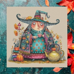 Puede incluir: Un diseño de punto de cruz de una bruja caprichosa disfrutando del té. La bruja lleva un sombrero grande y ropa estampada, rodeada de hojas de otoño, calabazas y una tetera. La paleta de colores incluye verde azulado, naranja y marrón.