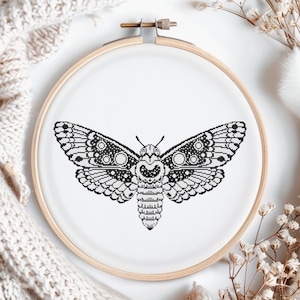 May include: Black and white embroidery hoop with a detailed moth design. The moth has a large, intricate body and wings with a circular pattern.