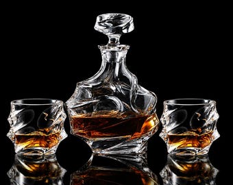 May include: A clear glass decanter with a matching stopper and two matching tumblers, all featuring a distinct, irregular, swirling textured surface. The decanter and glasses are filled with an amber-colored liquid against a black background.