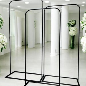 May include: Three black metal arch stands of different sizes. The stands are made of thin metal tubing and have a rectangular base.
