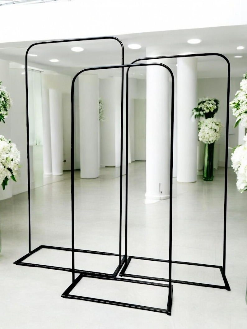 May include: Three black metal arch stands of different sizes. The stands are made of thin metal tubing and have a rectangular base.