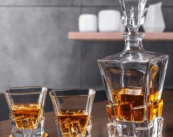 May include: A set of three clear glass decanter and whiskey glasses. The decanter has a square base and a tall, slender neck. The glasses are square and have a textured design. The decanter and glasses are filled with amber-colored liquid.