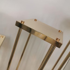 May include: Gold metal stand with a square top and four legs. The stand is made of metal and has a polished finish.