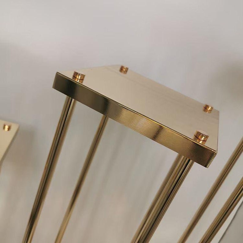 May include: Gold metal stand with a square top and four legs. The stand is made of metal and has a polished finish.