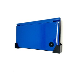 Puede incluir: Una consola de juegos portátil Nintendo DS Lite azul montada en una pared con un soporte negro.
