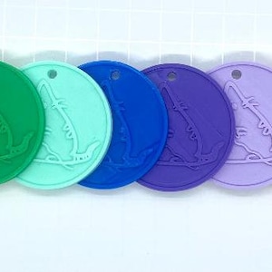 Può includere: Un set di dieci etichette rotonde in silicone con un design a coccodrillo in rilievo. Le etichette sono in un arcobaleno di colori, tra cui rosso, arancione, giallo, verde, blu, viola, rosa, bianco, nero e marrone.
