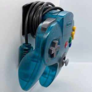 May include: A teal blue Nintendo 64 controller with a black cord and a gray control pad. The controller has a Nintendo logo and colored buttons.