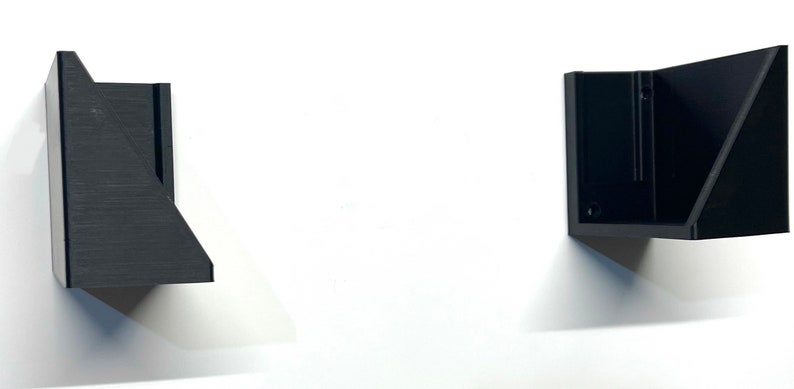 Puede incluir: Dos estanter&iacute;as de pared geom&eacute;tricas negras montadas en una pared blanca. Las estanter&iacute;as tienen un dise&ntilde;o angular moderno con forma triangular. Las estanter&iacute;as est&aacute;n hechas de un material negro mate y proyectan sombras en la pared.