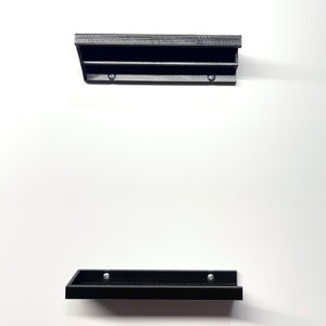 K&ouml;nnte beinhalten: Zwei schwarze Wandregale mit einer strukturierten Oberfl&auml;che. Die Regale sind aus Kunststoff und haben ein schlichtes Design.