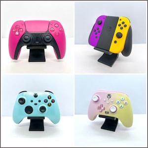 May include: Four different colored video game controllers on black stands. The controllers are pink, purple and yellow, light blue, and pink and yellow.
