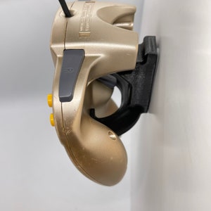 May include: A gold-coloured video game controller with yellow buttons and a black wall mount. The controller is mounted on the wall with the R button facing the camera.
