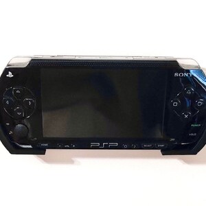 Peut inclure: Une console de jeu portable Sony PSP noire avec un &eacute;cran, des boutons et un pav&eacute; tactile. La console est fix&eacute;e au mur.