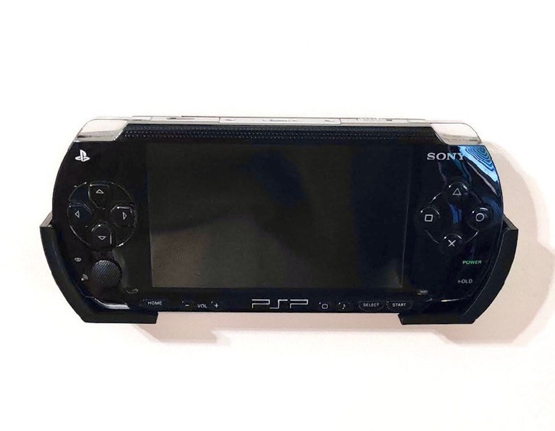 Peut inclure: Une console de jeu portable Sony PSP noire avec un &eacute;cran, des boutons et un pav&eacute; tactile. La console est fix&eacute;e au mur.