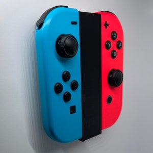 May include: A blue and red Nintendo Switch Joy-Con controller set with black buttons and a black centre piece. The controllers are attached to a black stand.