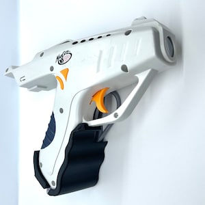 Può includere: Pistola giocattolo in plastica bianca con grilletto arancione e impugnatura nera. La pistola ha la scritta "Max Catz" stampata sul lato.