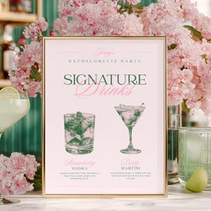 以下が含まれることがあります： 「Signature Drinks」の文字が緑とピンクで書かれた、独身最後のパーティー用の額入りサイン。サインには、ウォッカドリンクとダーティマティーニの2種類のカクテルのイラストが描かれています。ライムウェッジの入ったカクテルグラスが前景にあります。