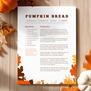 Peut inclure: Une recette de pain à la citrouille est imprimée sur papier blanc, avec ingrédients et instructions en marron. Le papier est décoré de feuilles d'automne et de citrouilles orange et marron. La recette est sur une surface en bois.