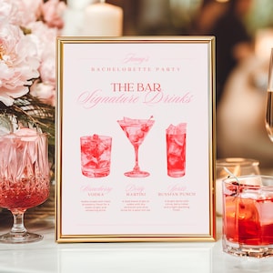 以下が含まれることがあります： 金色のフレームに入った看板には「Jenny's Bachelorette Party」と「The Bar Signature Drinks」と書かれています。看板には、ストロベリーウォッカ、ダーティマティーニ、ロシアンパンチの3種類のカクテルのイラストが描かれています。ピンク色のグラスとカクテルグラスが前景にあります。