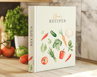 May include: A white recipe binder with a green and white floral design featuring vegetables like carrots, onions, peppers, and broccoli. The binder has the text "Olivia's RECIPES" on the front.