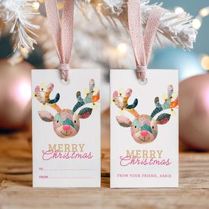 May include: Two white rectangular Christmas gift tags with a reindeer design. The reindeer has colorful patchwork antlers and a pink nose. The words "Merry Christmas" are written in pink script. One tag has "To" and "From" lines.