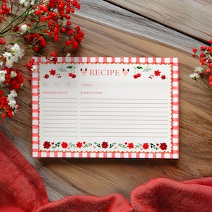 May include: A recipe card with a red and white gingham border and cherry illustrations. The card has spaces for ingredients, title, and directions. Red flowers and a red cloth are in the background.