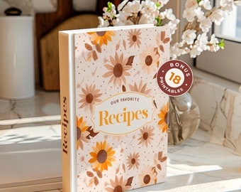 Peut inclure: Un classeur de recettes blanc avec un motif floral composé de tournesols et de feuilles. Le classeur porte l'inscription "Nos recettes préférées" sur la face avant. Un autocollant sur la face avant indique "Bonus 18 imprimés".