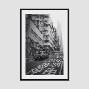 Op de afbeelding: Zwart-witfoto van een stadsstraat. Een taxi rijdt over de weg, met gebouwen aan weerszijden. De woorden "KEEP CLEAR" zijn op de weg geschilderd.